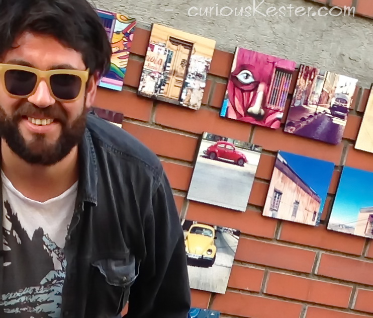 a guy with sunglasses and his artworks hanging from a wall